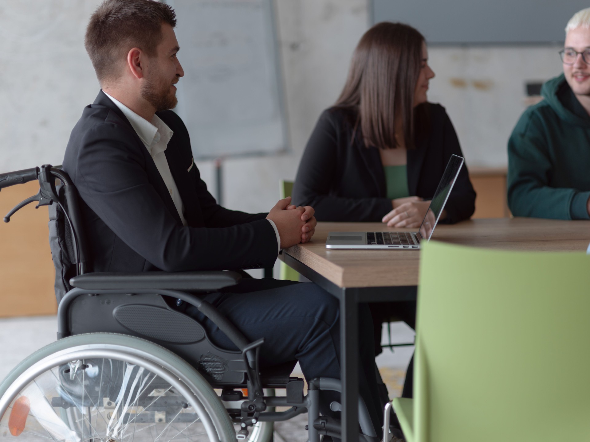 Photo en gros plan d’un groupe diversifié de professionnels, y compris une personne handicapée, réunis dans un bureau moderne pour une réunion productive et inclusive.
