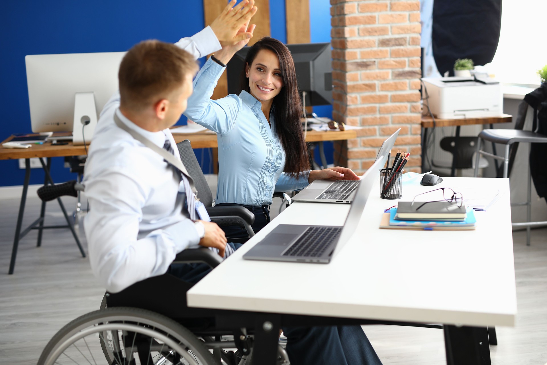 L’homme d’affaires handicapé s’assied dans le fauteuil roulant à la table de travail dans le bureau et salue la femme d’affaires.
